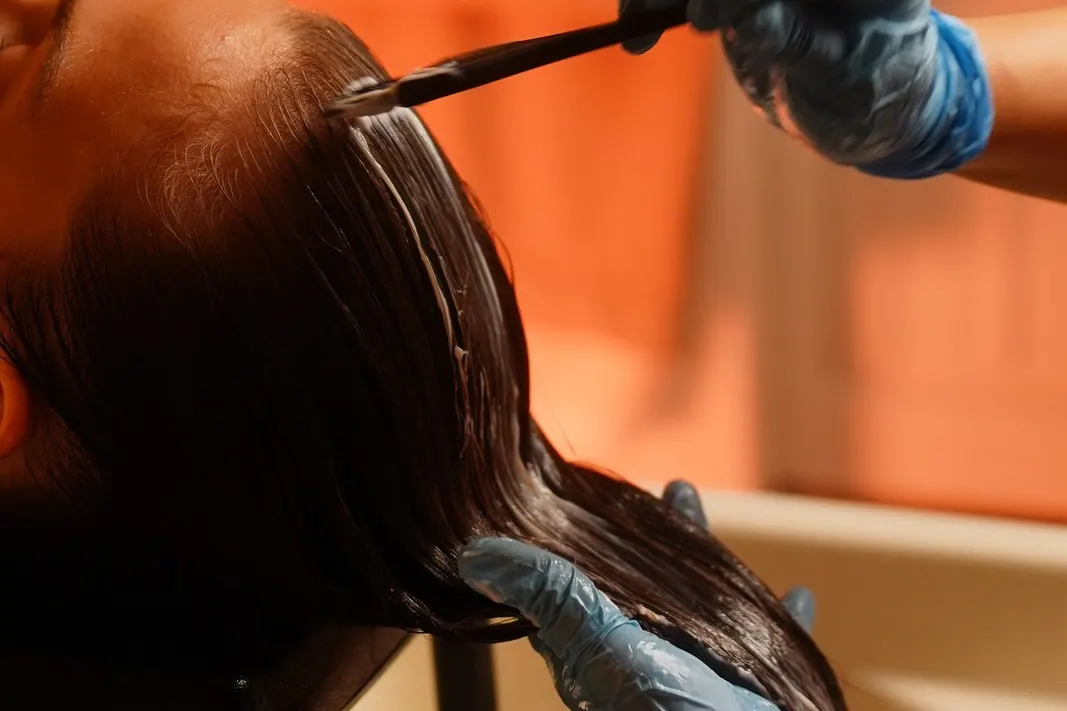 A head spa therapist brushes a nourishing scalp and hair treatment onto a reclining client's hair at the wash basin